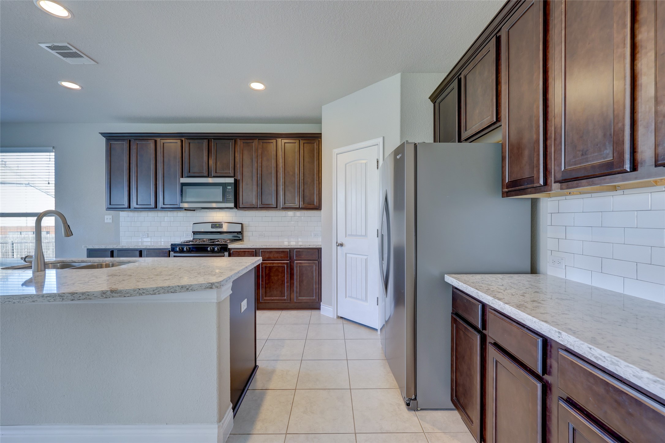 431 Millard Street Georgetown, TX 78628 - Photo 11 of 36 Kitchen featuring stainless steel appliances, light stone counters, light tile patterned floors, dark wood finish cabinetry, and recessed lighting