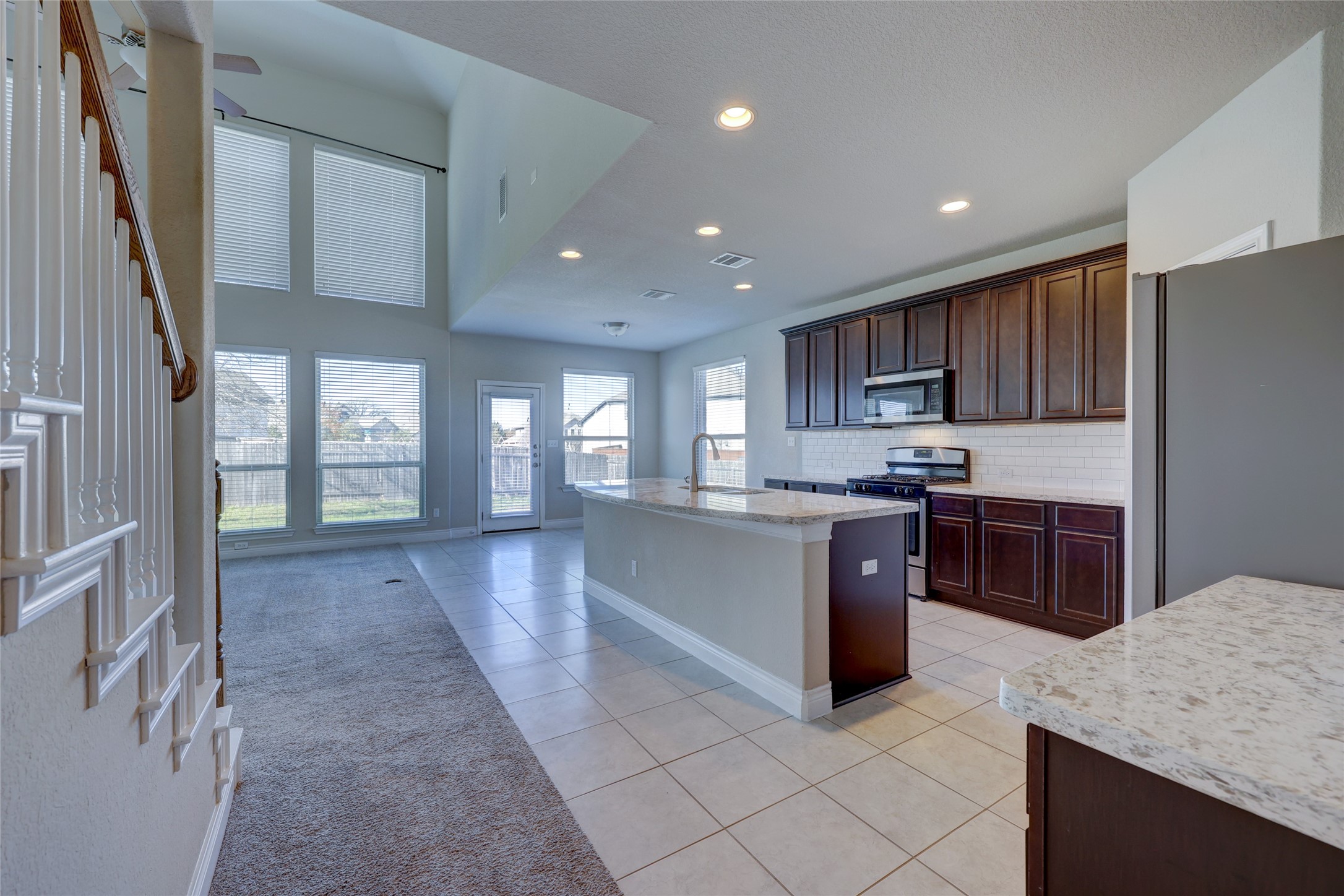 431 Millard Street Georgetown, TX 78628 - Photo 10 of 36 Kitchen featuring a center island with sink, stainless steel appliances, light tile patterned floors, dark wood finish cabinetry, and light stone counters