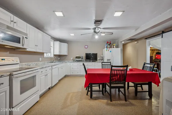 a kitchen with stainless steel appliances kitchen island granite countertop a dining table chairs sink and white cabinets