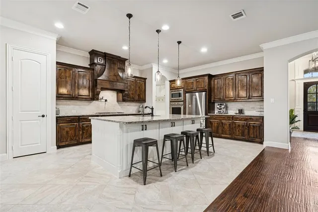 a kitchen with stainless steel appliances kitchen island granite countertop a stove a sink a oven a dining table and chairs with wooden floor