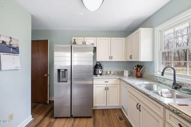 a kitchen with stainless steel appliances granite countertop a refrigerator a sink a stove and white cabinets with wooden floor