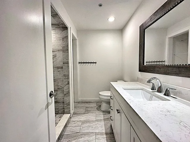 a bathroom with a granite countertop sink a mirror and a toilet