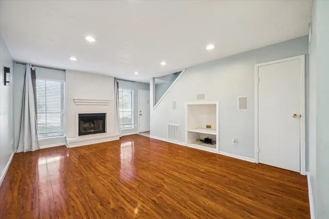 a view of an empty room with wooden floor fireplace and a window
