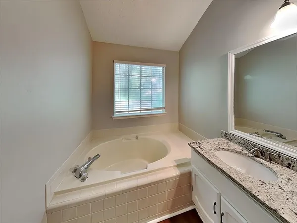 a bathroom with a granite countertop tub sink and mirror