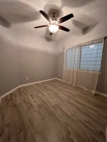 an empty room with wooden floor fan and windows