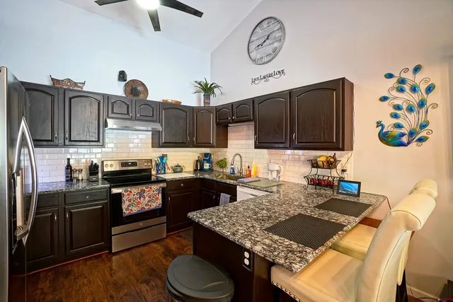 a kitchen with stainless steel appliances granite countertop a stove top oven a sink a dining table and chairs with wooden floor