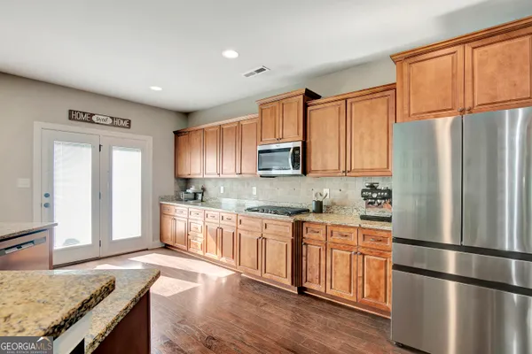 a large kitchen with stainless steel appliances a stove a refrigerator a oven and white cabinets with wooden floor