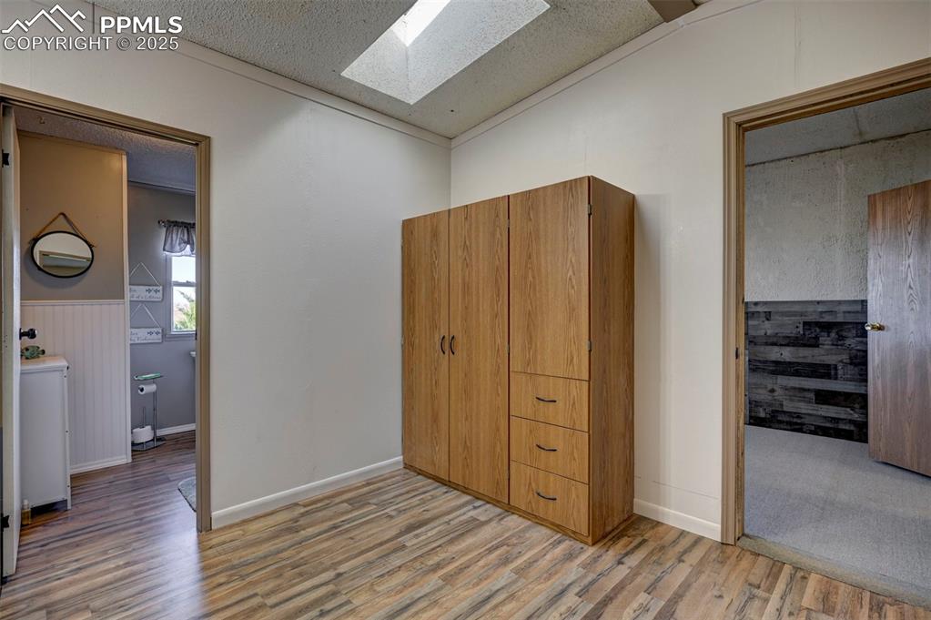 35355 Funk Road Calhan, CO 80808 - Photo 22 of 31 Bedroom featuring light wood-style floors, a skylight, a textured ceiling, wainscoting, and ornamental molding