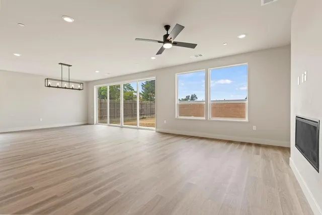an empty room with wooden floor fan and windows