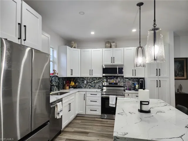 a kitchen with stainless steel appliances kitchen island granite countertop a refrigerator a stove a sink and white cabinets