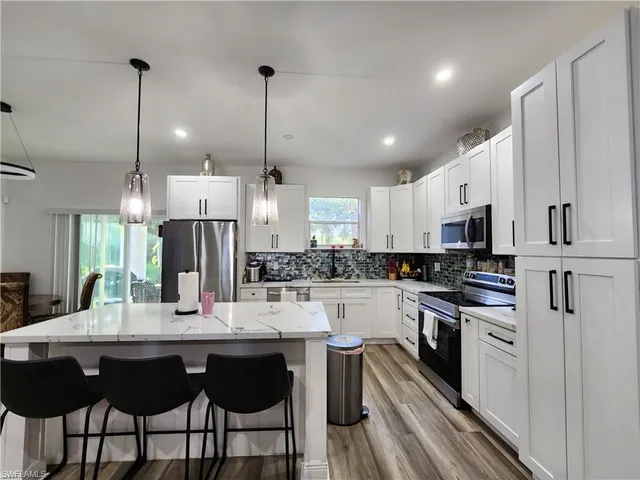 a kitchen with stainless steel appliances kitchen island granite countertop a sink a stove a refrigerator and island with wooden floor