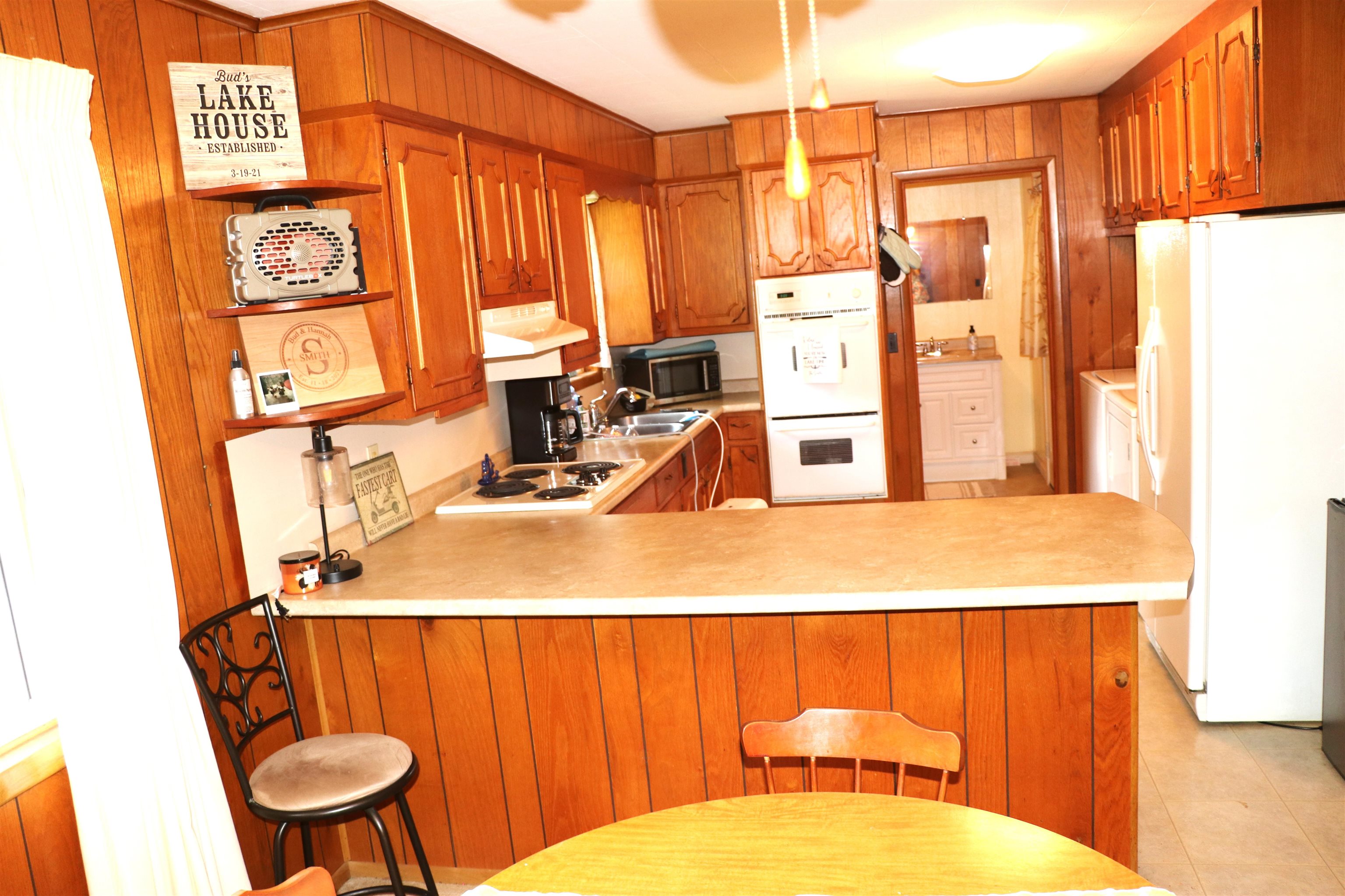 160 Patrick Drive Springville, TN 38256 - Photo 7 of 34 Kitchen featuring wood-paneled walls, wood-finish cabinetry, a built-in oven, and a breakfast bar with a light-toned countertop