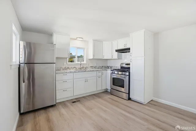 a kitchen with a refrigerator stove and white cabinets with wooden floor