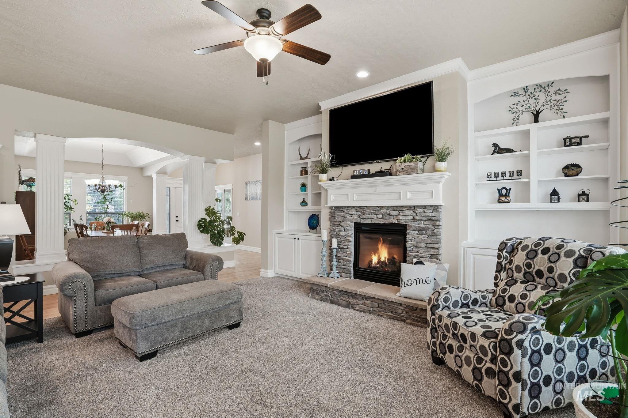 3969 North Hollymount Way Meridian, ID 83646 - Photo 8 of 47 Living area featuring a stacked stone fireplace with an integrated mantel, built-in shelving, a ceiling fan, recessed lighting, and a broad archway opening to a dining space with wood-finish flooring