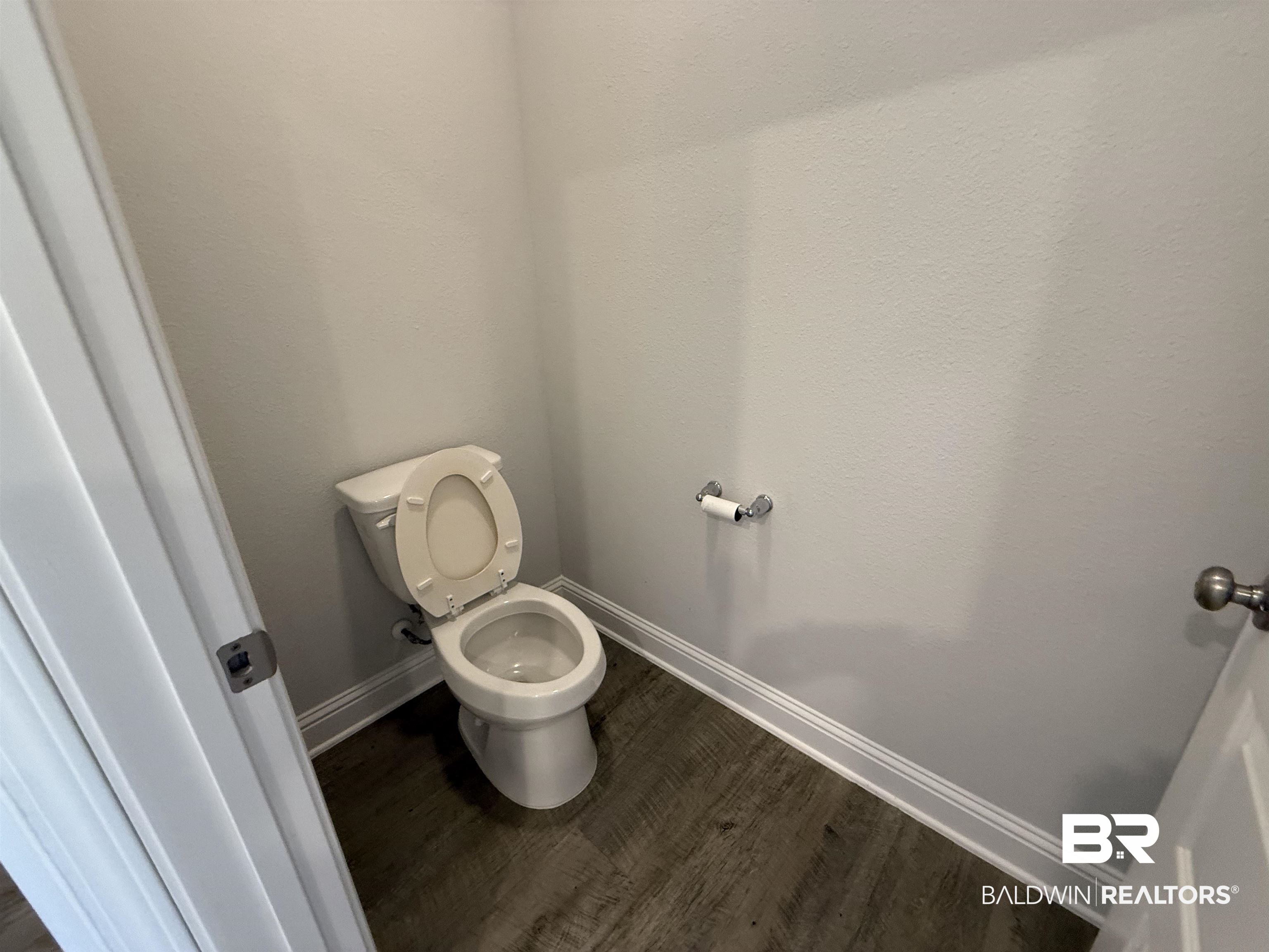 23247 Lieutenant Avenue Foley, AL 36535 - Photo 36 of 47 Powder room with a white toilet, wood-finish flooring, light gray walls, white baseboards, and a chrome toilet paper holder