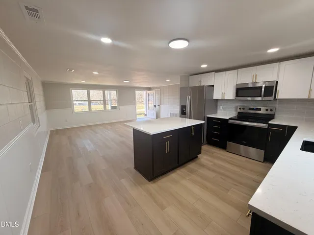 a large kitchen with stainless steel appliances granite countertop a large counter top a sink a refrigerator and a stove