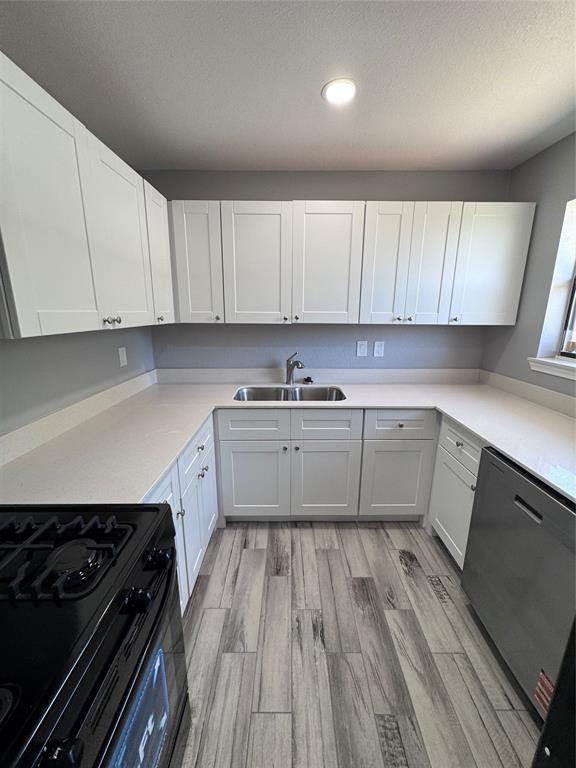 1736 Ransom Terrace Fort Worth, TX 76112 - Photo 2 of 27 U-shaped kitchen featuring white shaker cabinetry, light-toned countertops, a double basin stainless steel sink, and wood-finish flooring