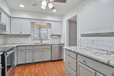 a kitchen with a sink dishwasher a stove and white cabinets with wooden floor