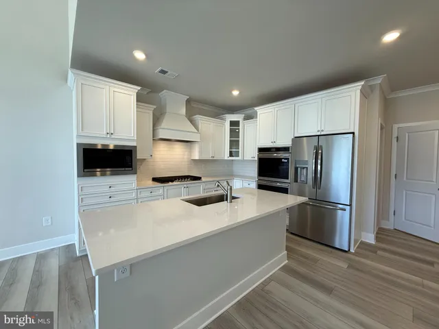 a large kitchen with stainless steel appliances kitchen island granite countertop a large stove a refrigerator a sink dishwasher and white cabinets with wooden floor