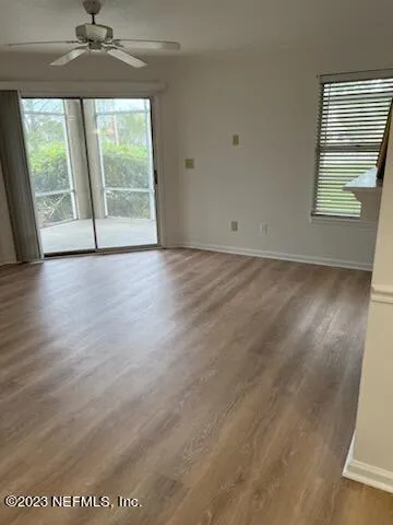 an empty room with wooden floor fan and windows