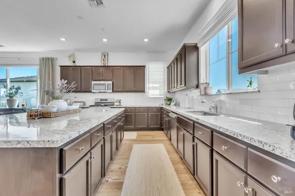a kitchen with stainless steel appliances granite countertop a refrigerator a stove top oven a sink dishwasher and white cabinets with wooden floor
