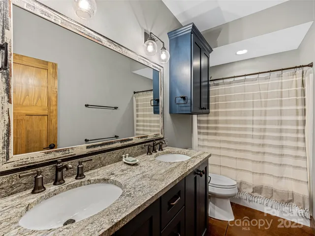 a bathroom with a granite countertop sink a toilet a mirror and shower curtain