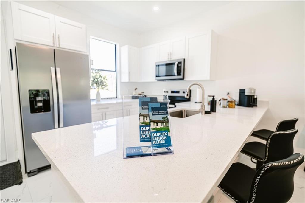 907 Homestead Road South Lehigh Acres, FL 33974 - Photo 9 of 43 Modern kitchen featuring a large white countertop island with integrated sink, stainless steel appliances, white cabinetry, and recessed lighting