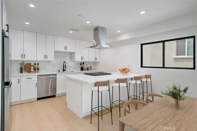 a kitchen with stainless steel appliances kitchen island a table chairs in it and white cabinets