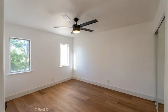 an empty room with wooden floor ceiling fan and windows