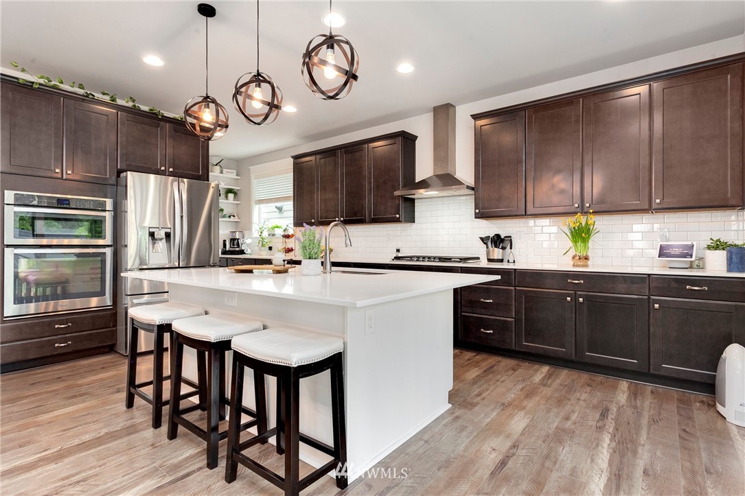 253 Field Place Southeast Renton, WA 98059 - Photo 16 of 40 a kitchen with stainless steel appliances granite countertop a stove a refrigerator a sink dishwasher a dining table and chairs with wooden floor
