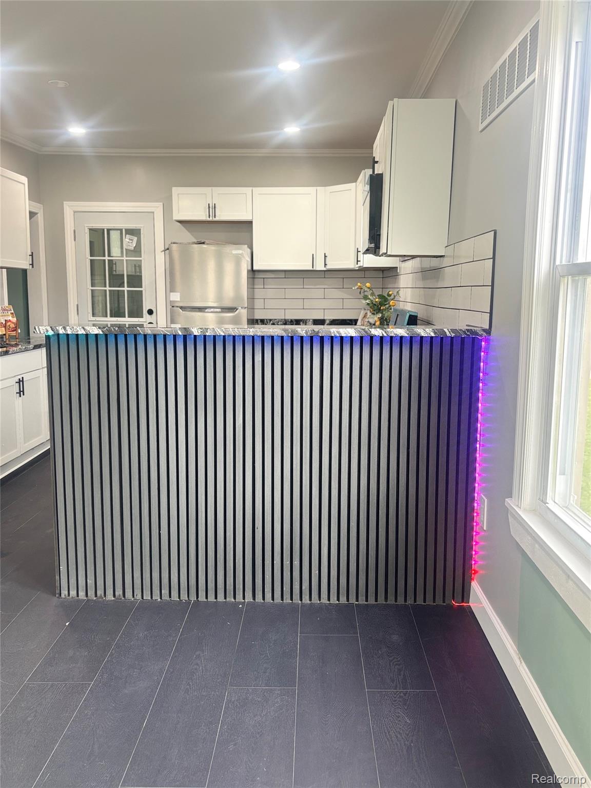 5012 Fischer Street Detroit, MI 48213 - Photo 6 of 22 Kitchen with white cabinetry, freestanding refrigerator, ornamental molding, a peninsula, and decorative back splash and bar with LED lights.