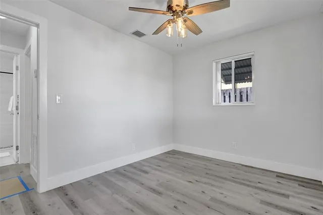 an empty room with wooden floor fan and windows