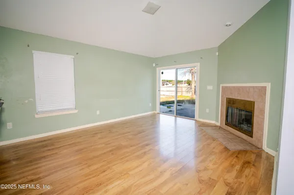 an empty room with wooden floor fireplace and windows
