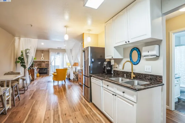 a kitchen with granite countertop a stove a sink dishwasher and white cabinets with wooden floor