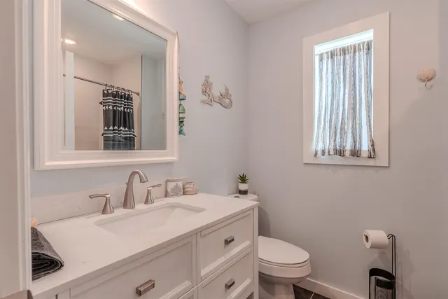 a bathroom with a toilet a sink a mirror a window and vanity