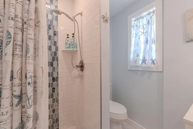 a bathroom with a granite countertop shower a toilet and a window