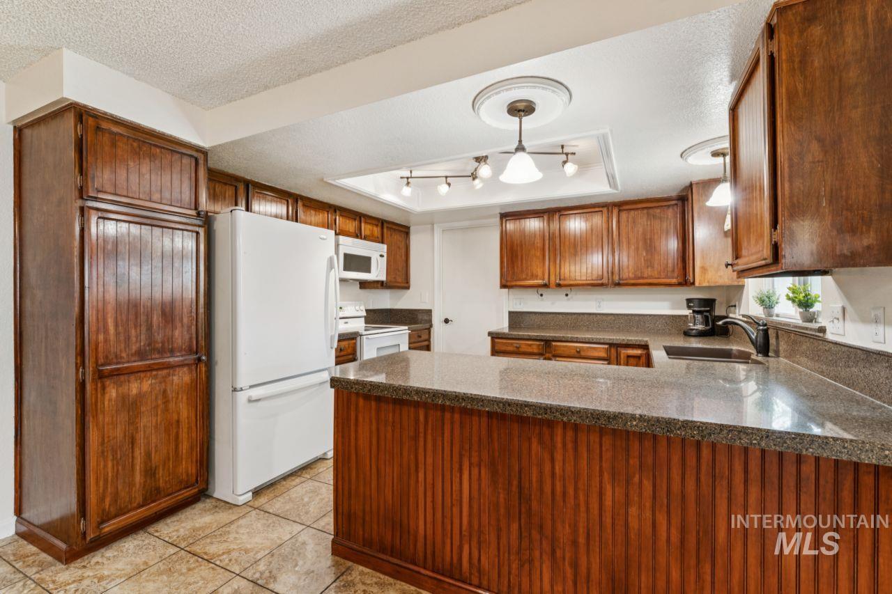 4093 North Marylebone Way Boise, ID 83713 - Photo 10 of 48 Kitchen featuring a textured ceiling, white appliances, wood finish cabinets, a tray ceiling, and a peninsula