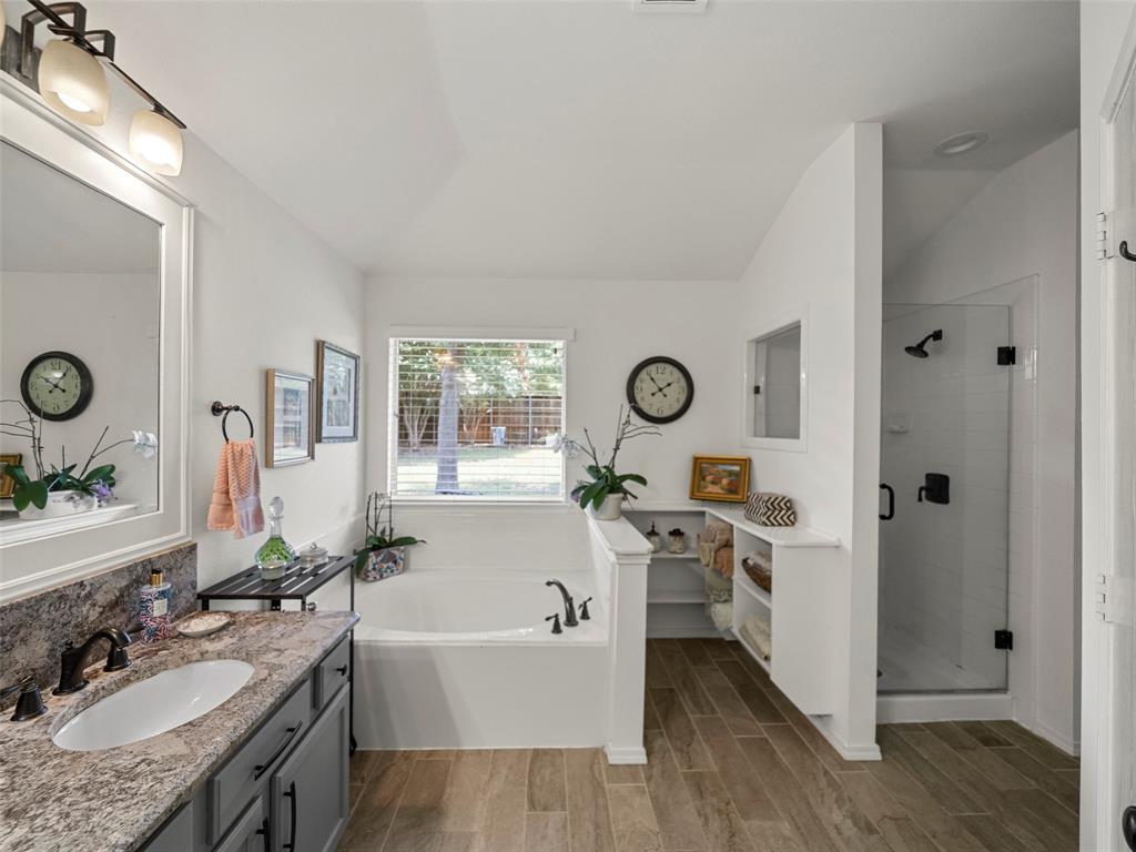 204 Arbor Ridge Drive Allen, TX 75002 - Photo 18 of 36 Spacious bathroom featuring a built-in soaking tub, separate glass-enclosed shower, wood-finish tile flooring, a window offering natural light, and a vanity with a stone countertop