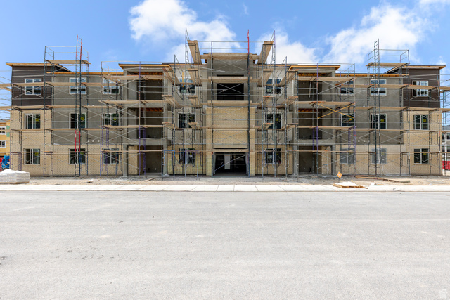 Multi-story building under construction, featuring multiple window openings, a mix of light-toned and dark-toned exterior finishes, and visible scaffolding