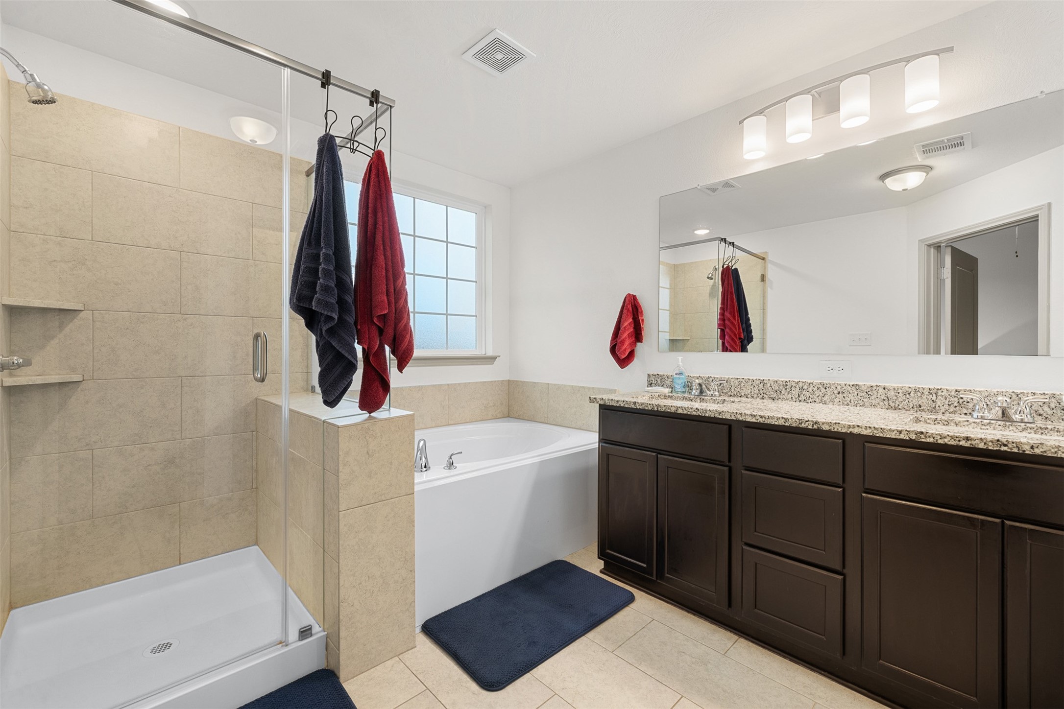 1968 Chief Street Bryan, TX 77807 - Photo 8 of 27 This modern bathroom features a spacious walk-in shower with glass doors, a large soaking tub, and a granite-topped vanity with dual sinks. Light tiles and dark cabinetry create a stylish contrast, with ample natural light from a frosted window.