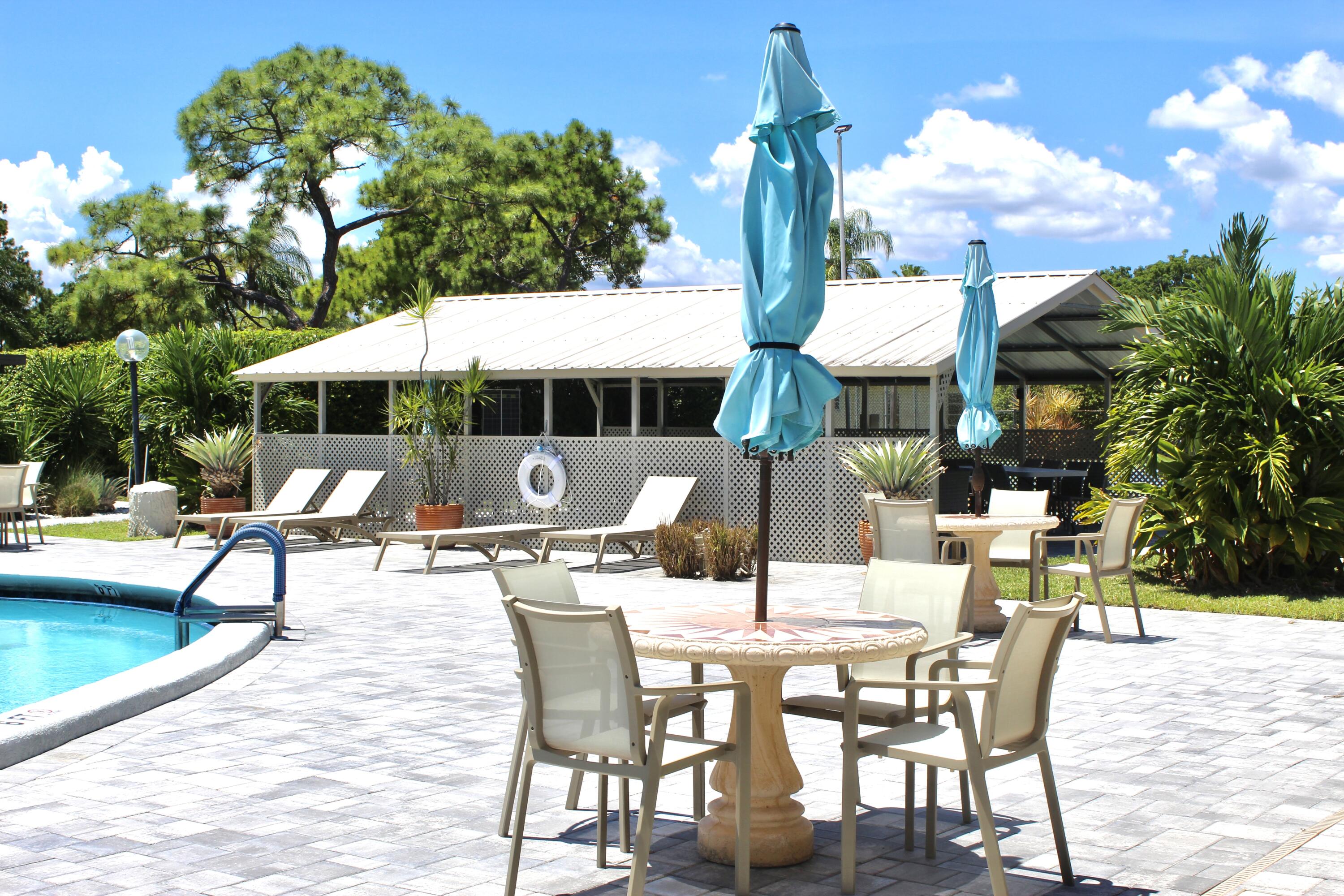 5130 Nesting Way, Unit C Delray Beach, FL 33484 - Photo 27 of 33 a view of a patio with a dining table and chairs under an umbrella with large trees