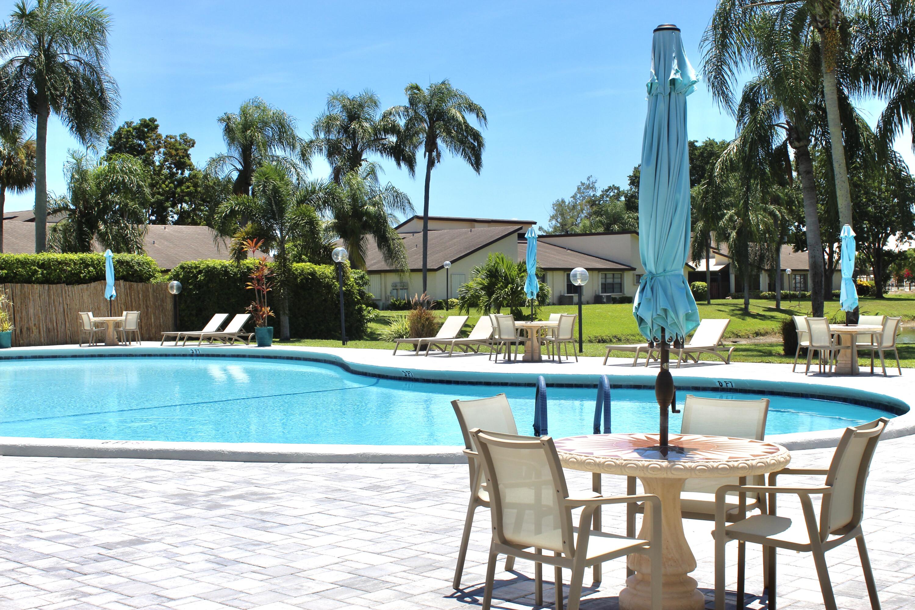 5130 Nesting Way, Unit C Delray Beach, FL 33484 - Photo 28 of 33 a view of a swimming pool with a table and chairs under an umbrella