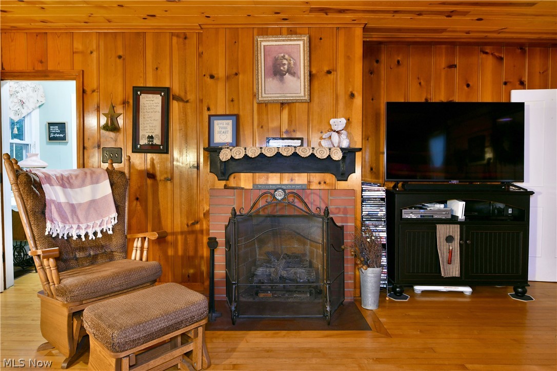 8683 King Graves Road Northeast Warren, OH 44484 - Photo 22 of 50 Brick fireplace with a black metal screen and an ornate mantel, set against wood-paneled walls and wood-finish flooring