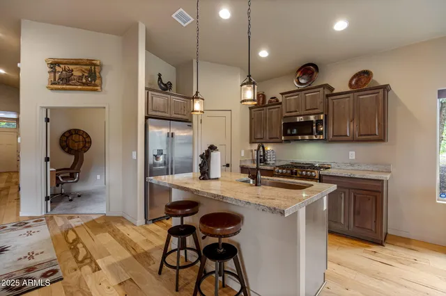 a kitchen with stainless steel appliances granite countertop a sink a refrigerator and a wooden floor