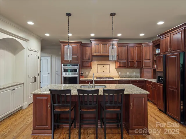 a kitchen with stainless steel appliances granite countertop a refrigerator a sink dishwasher a dining table and chairs with wooden floor