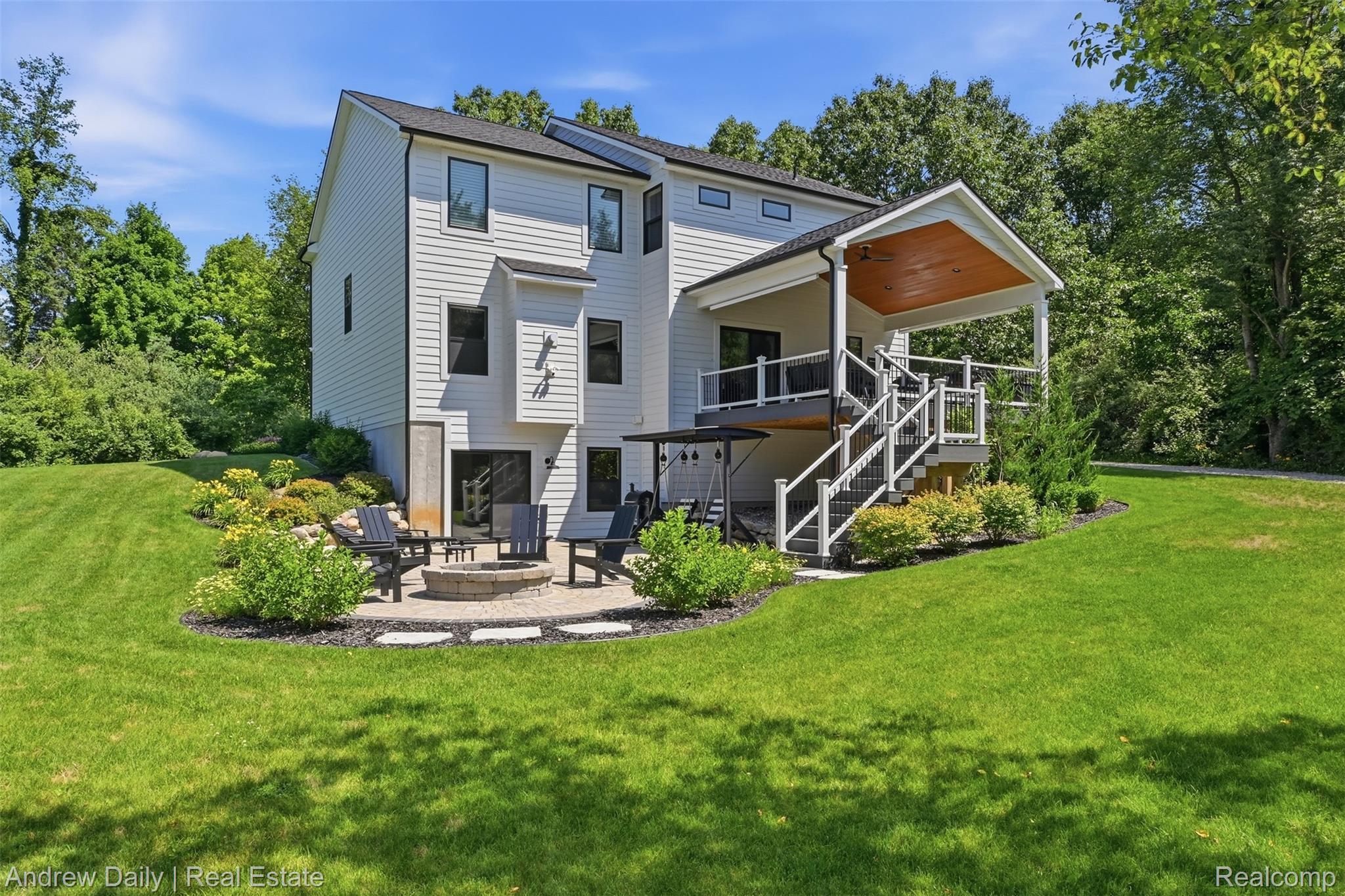4661 Spears Road Pinckney, MI 48169 - Photo 47 of 56 Rear exterior featuring white horizontal siding, a covered deck with a wood-finish ceiling, a stone paver patio with a built-in fire pit, and a spacious lawn