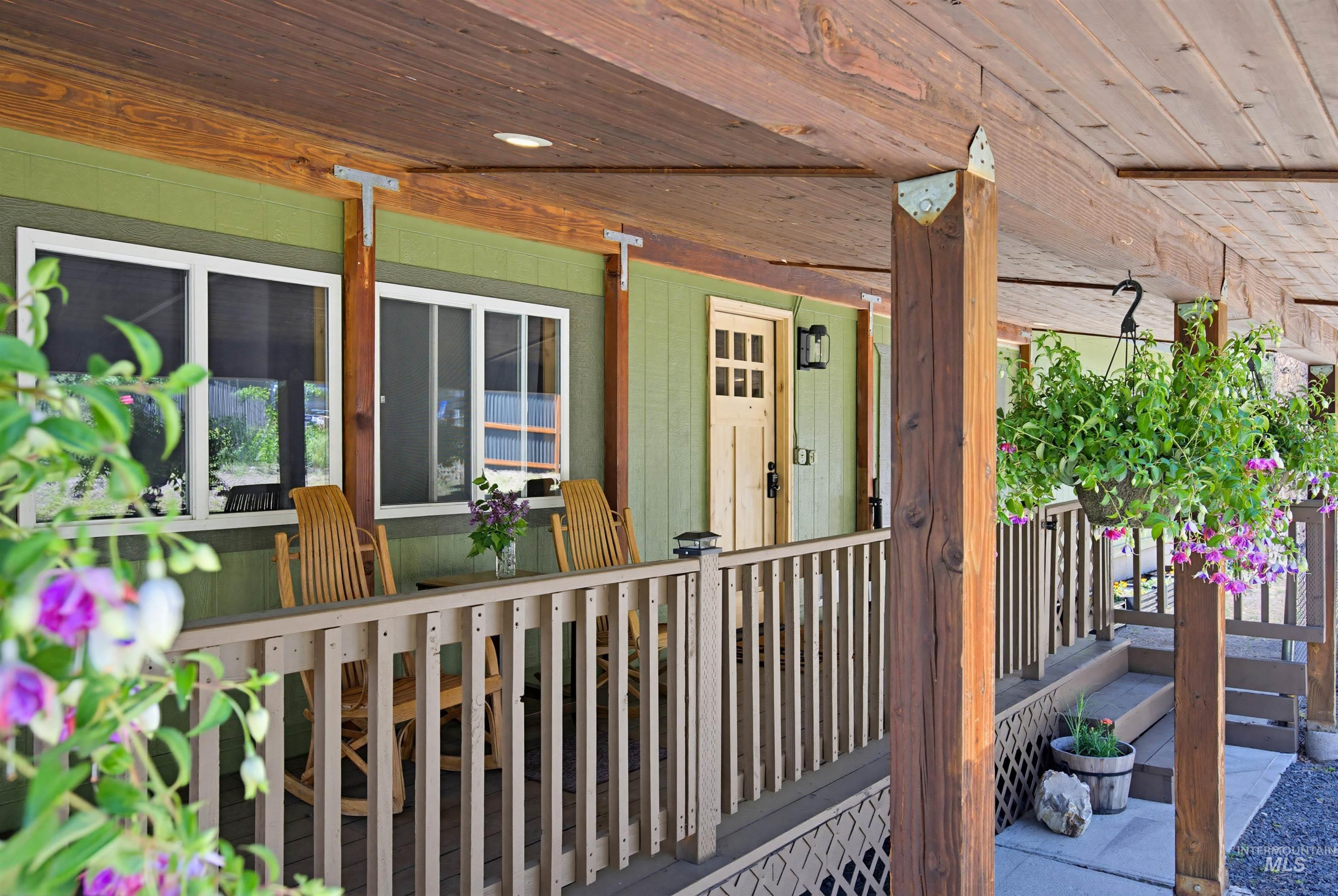 79 Sunset Loop Cascade, ID 83611 - Photo 3 of 44 Covered wooden porch featuring a light green exterior, multiple windows with white frames, a paneled entry door, and a black exterior light fixture