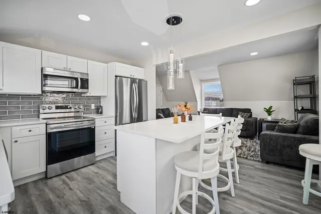 a kitchen with stainless steel appliances a stove a sink dishwasher a refrigerator and a dining table with wooden floor