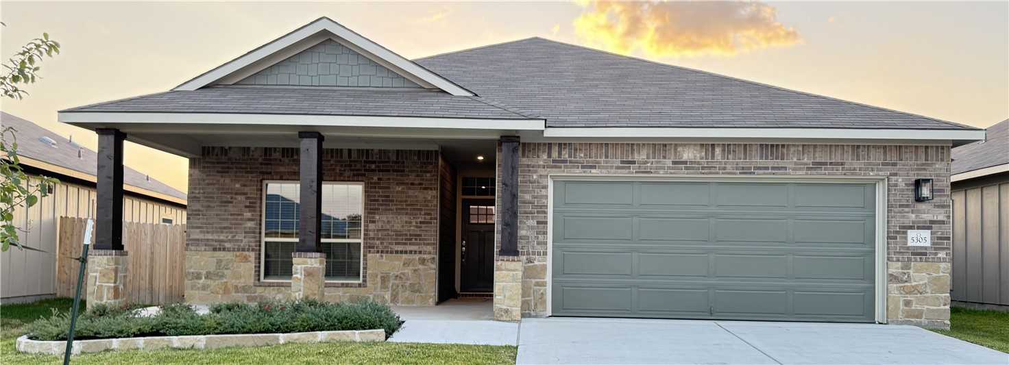 View of front of home featuring driveway, a shingled roof, an attached garage, brick siding, and stone siding