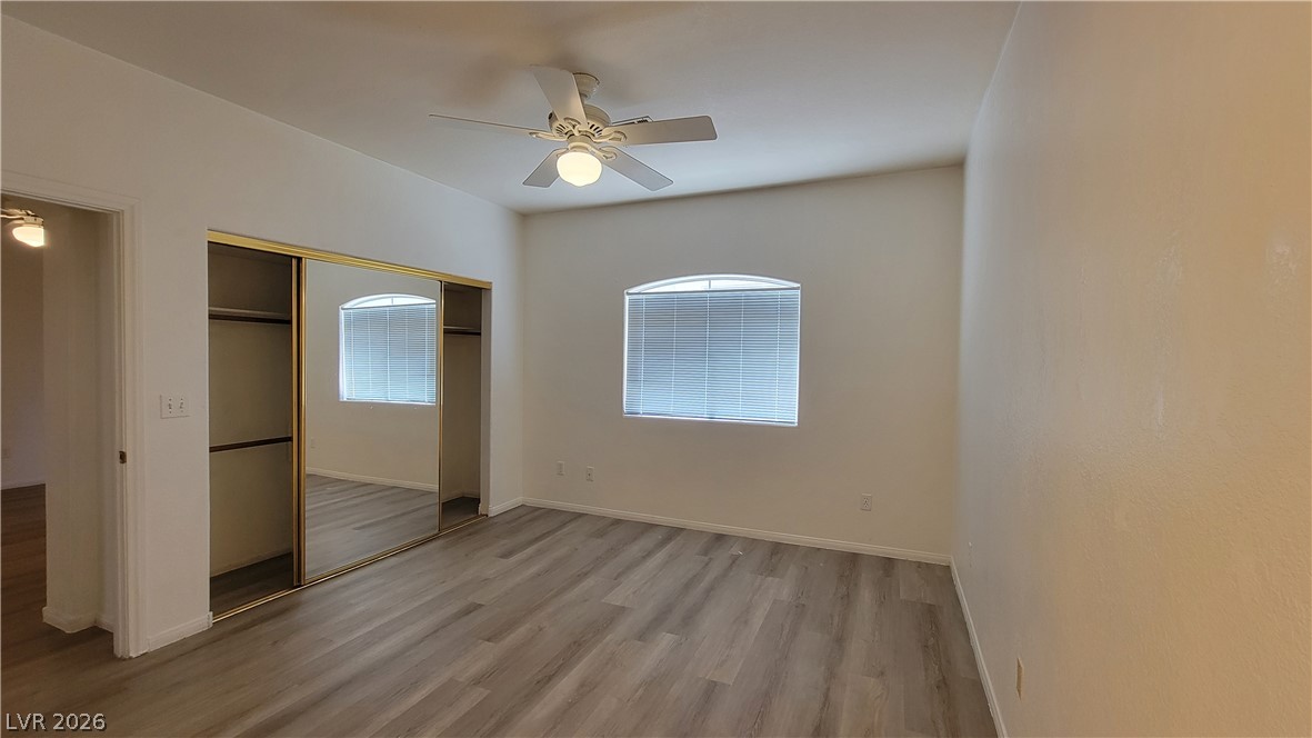 3320 South Fort Apache Road, Unit 111 Las Vegas, NV 89117 - Photo 4 of 12 A quiet bedroom with a ceiling fan, mirrored closet doors, and wood flooring.